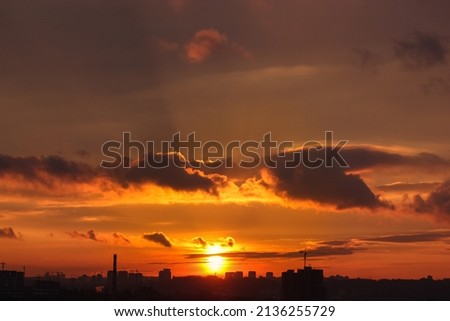 Kyiv, Ukraine. Silhouettes of houses against red-orange sky at sunset. City urban landscape. Contrasting clouds at sunset. The sun is setting behind the horizon. Sunlight breaking through the clouds.