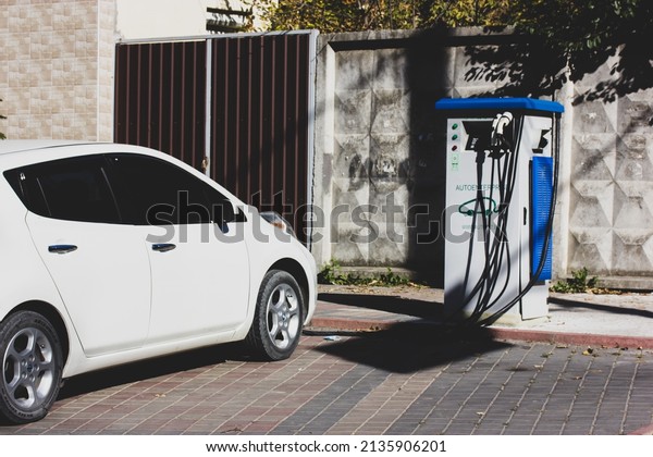 Kyiv, Ukraine. A white electric automobile is\
charging at EV charging station. Sedan car parked on a street.\
Travel by car concept. Green energy and eco power produced from\
sustainable source\
concept.