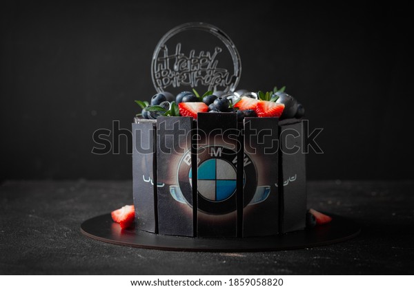 Kyiv/Ukraine-11.22.2020: Black cake with BMW logo on\
it with fruit and berries decoration on top. Birthday cake on the\
black background. BMW cars\
fan