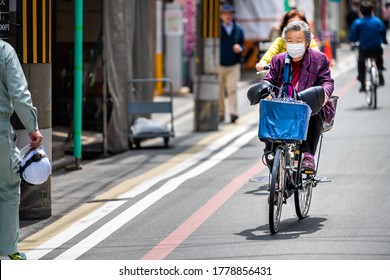 Kyoto, Japan - April 17, 2019: Kyoto downtown district with people local Japanese senior elderly person wearing mask face covering riding bicycle bike and shopping basket
