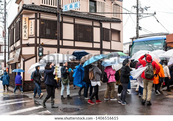 Kyoto, Japan - April 9, 2019: Many group of people\
with umbrellas crossing street during rainy day towards\
Kiyomizu-dera temple