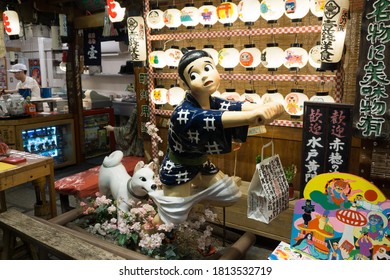 Kyoto, Kyoto Prefecture, Japan - March 14 2018: Famous Statue Of Dog Biting The Pants Of A Child That Stands At The Entrance Of The Famous Okonomiyaki Restaurant, Issen Yoshoku. Photo Taken In Night.