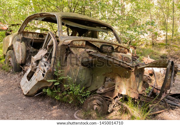 KYRKO MOSSE, RYD, SMALAND,\
SWEDEN - JUNE 23 2019: Historical junkyard / car cemetery in\
southern part of Sweden. Front of rusty car wreck, half embedded in\
forest moss.