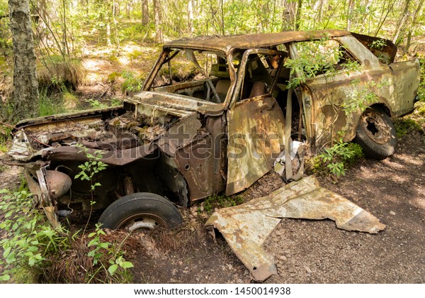 KYRKO MOSSE,\
RYD, SMALAND, SWEDEN - JUNE 23 2019: Historical junkyard / car\
cemetery in southern part of Sweden. Side view of green rusty car\
wreck, half embedded in forest\
moss.