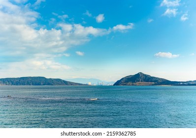 kyushu, fukuoka - december 07 2021: Seascape view of the Fukuoka Tower between the Imazu coast on right and the Nokono Island on left from the Fukuokashi Umizuri Park with Mount Hōman in background.