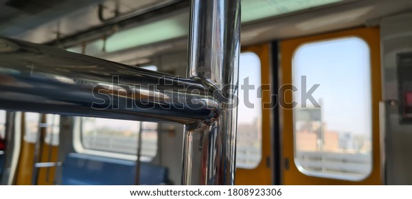 L shaped metal bar inside an underground subway
train  for standing people to hold, also act a separator between
train sections. Orange doors with glasses, blue seats and white
walls in the morning.