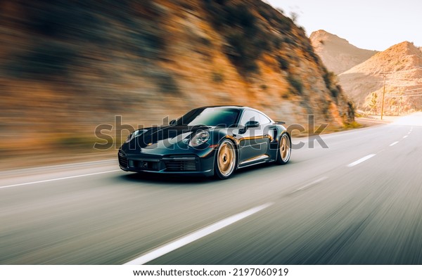 LA, CA, USA\
August 12,\
2022\
Porsche Turbo S driving on the street by itself next to a\
rock face