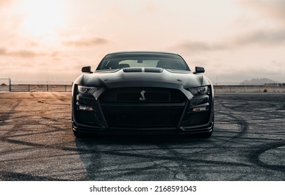 LA, CA, USA
May 19, 2022
Black Mustang Shelby Cobra Parked Head-on Showing The Front Of The Car With Clear Skies Overhead