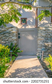 La Jolla, California- Painted Gray Single Gate In Between Stone Wall. Entrance Of A Fenced House With Garden Lights At The Front Near The Plants And A View Of A Painted White House At The Back.