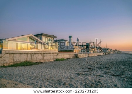 La Jolla, California- Row of beach houses near the sandy seashore during sunset. There is a sandy shore of the beach on the right near the houses with reflective glass fence and windows.