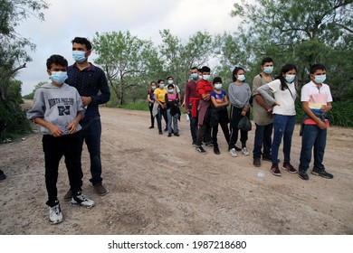 La Joya, TX, USA - May 26, 2021:  A  Central American Man And His Son Who Crossed The Rio Grande River Illegally To Request Asylum Wait In Front Of A Line Of Unaccompanied Minors.