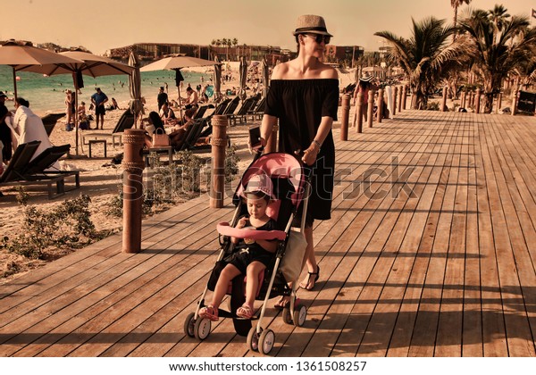 La\
Mer in Dubai, UAE - May 06, 2018: Mom with baby on the beach La Mer\
at sunset.  It is a new beachfront district with shopping and\
restaurants in Jumeirah. DUBAI, UAE -May 06, 2018\
.