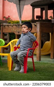 La Paz, Bolivia - September 10 2022: A Bolivian Boy Is Sitting Outside In A Red Plastic Chair