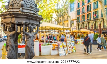 La Rambla sunny street with many walking people. La Rambla - most popular pedestrian street in Barcelona. Selective focus on drinking water fountain on foreground.