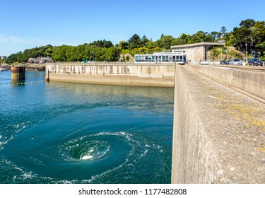 La Richardais, France - June 23, 2018: The Turbines Of The River Rance Tidal Power Station, Run By French Public Electricity Utility Company EDF, Generate Whirlpools At The Surface Of The Water.