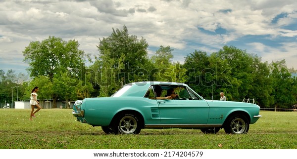 La Tour de Salvagny,\
Rhone Alpes France\
05 25 2022\
Beautiful ford mustang car from the\
sixties rolling in a park on a summer day with in the background an\
impressive sky