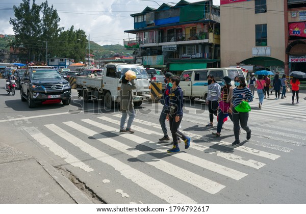 La Trinidad, Benguet, Philippines - July 17, 2020:\
Cars stop as people with face masks cross and walk on the\
pedestrian lane. This image shows 100% face mask usage at least in\
this area of the town.