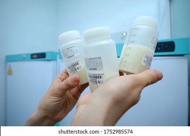 Lab Assistant Hand Holding Breast Milk Storage Containers With Human Milk, Freezers On The Background. Human Milk Bank Laboratory