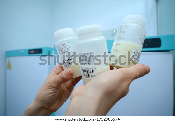 Lab assistant hand holding breast milk storage\
containers with human milk, freezers on the background. Human Milk\
Bank laboratory