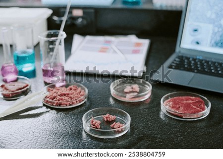 Lab setup showing multiple food samples, scientific instruments, and a laptop for conducting analysis and recording results. Various meat samples on petri dishes are present
