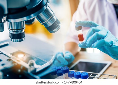 Lab Technician Assistant Analyzing A Blood Sample In Test Tube At Laboratory With Microscope. Medical, Pharmaceutical And Scientific Research And Development Concept.