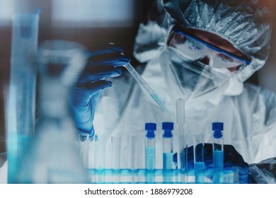 Lab technician in white overalls, blue gloves and safety goggles pipetting out liquid substance to test tubes in line. Scientist using labware while developing anti-coronavirus vaccine or treatment