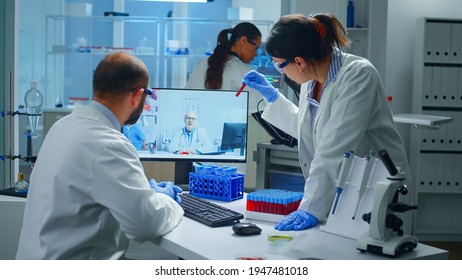 Lab Technicians Talking On Video Call With Professional Chemist Doctor Explaning Vaccine Reactions, Woman Nurse Showing Blood Sample On Web Cam, During Virtual Meeting In Medical Research Laboratory