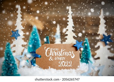 Label With English Text Merry Christmas And Happy 2022. Christmas Trees With Star Decoration And Ornament. Brown Rustic Wooden Background With Snow And Snowflakes