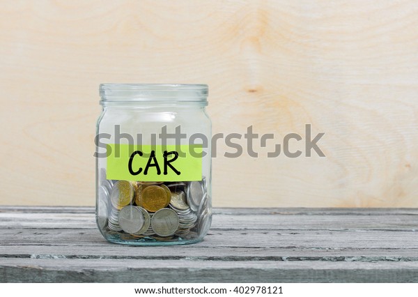 Label on a glass\
jar with the inscription - car. Glass jar with coins. Financial\
concept on wooden\
background