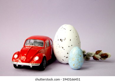 Labinsk. Russia. 25.03.2021 Next To The Red Car Are Two Easter Eggs On A Yellow Background. Easter And Travel Concept. Easter And Family Fun.