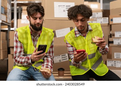 Labor or communication concept. Happy young colleagues eating lunch and using smartphones while working in distribution warehouse. Copy space - Powered by Shutterstock