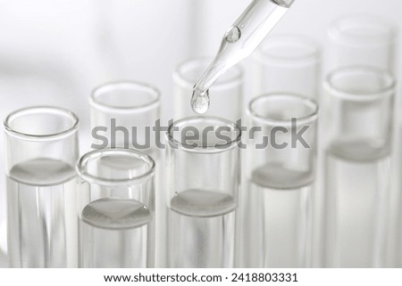 Laboratory analysis. Dripping liquid from pipette into glass test tube on blurred background, closeup