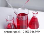 Laboratory analysis. Dripping red liquid into beaker on white table, closeup