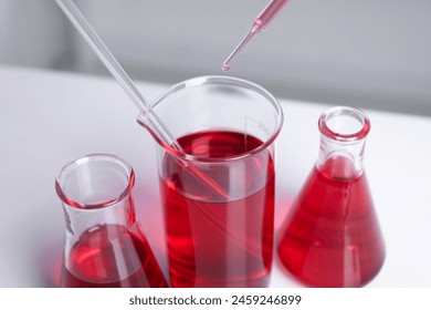 Laboratory analysis. Dripping red liquid into beaker on white table, closeup - Powered by Shutterstock