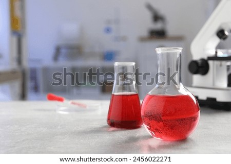 Laboratory analysis. Flasks with red liquid, petri dish and microscope on light grey table