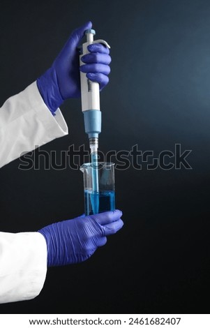 Laboratory analysis. Scientist dripping sample with micropipette into beaker on dark background, closeup