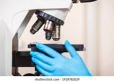 laboratory assistant in blue gloves examines a semen sample under a microscope. Shallow depth of field, close-up. Medical research virus center in grayscale.