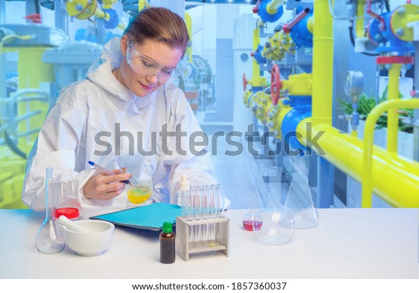 Laboratory assistant at a chemical factory.\
Girl works in laboratory. Woman chemist near pipes. Laboratory\
assistant is writing something. Chemist takes samples at the\
factory. Scientific\
experiments