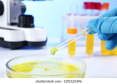 Laboratory assistant dripping urine sample for analysis from pipette into petri dish on table, closeup