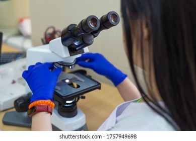 laboratory assistant is looking through a microscope. Close-up doctor laboratory assistant looking through a microscope, determining a blood test of a patient, red blood cells