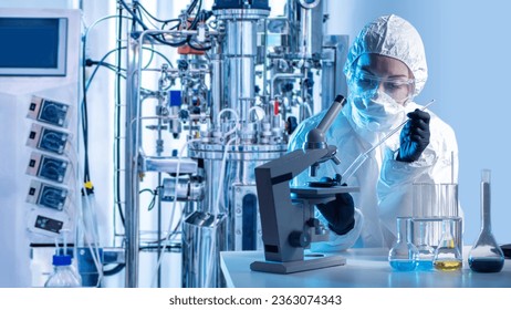 Laboratory assistant with microscope bio tech. Biologist at work. Scientist near bioreactor. Biologist in protective suit. Laboratory assistant makes scientific experiment. Biologist with flask