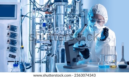 Laboratory assistant with microscope bio tech. Biologist at work. Scientist near bioreactor. Biologist in protective suit. Laboratory assistant makes scientific experiment. Biologist with flask