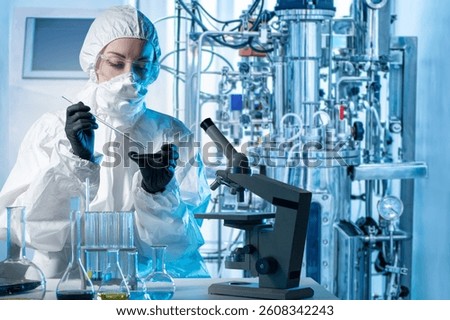 Laboratory assistant with microscope bio tech. Biologist at work. Scientist near bioreactor. Biologist in protective suit. Laboratory assistant makes scientific experiment. Biologist with flask