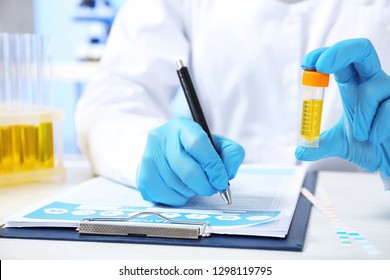 Laboratory assistant with urine sample for analysis writing medical report at table, closeup
