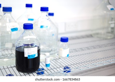 Laboratory bottles on wire shelf mostly empty with one filled with dark liquid. Lab workflow labels left blank.