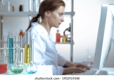 laboratory equipment, supplies, jars, bottles, cylinders, beakers, graduate, test-mixer, medicine-glass. Active lady scientist is typing on the keyboard of a computer and looking at the display in a c