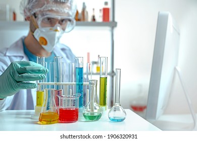 laboratory equipment, supplies, jars, bottles, cylinders, beakers, graduate, test-mixer, medicine-glass. A chemistry laboratory assistant in protective goggles and a mask examines test tubes