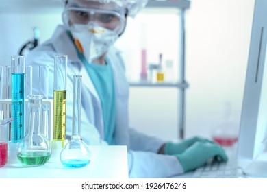 laboratory equipment, supplies, jars, bottles, cylinders, beakers, graduate, test-mixer, medicine-glass. Chemistry laboratory assistant in protective goggles and a mask examines test tubes.