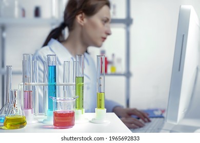 laboratory equipment, supplies, jars, bottles, cylinders, beakers, graduate, test-mixer, medicine-glass. An active lady scientist is typing on the keyboard of a computer and looking at the display