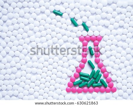 Laboratory flask contained solution made by pink pills and green capsules on white tablets background. Creative idea for new drugs, pharmaceutical analysis, research development and chemical concept.
